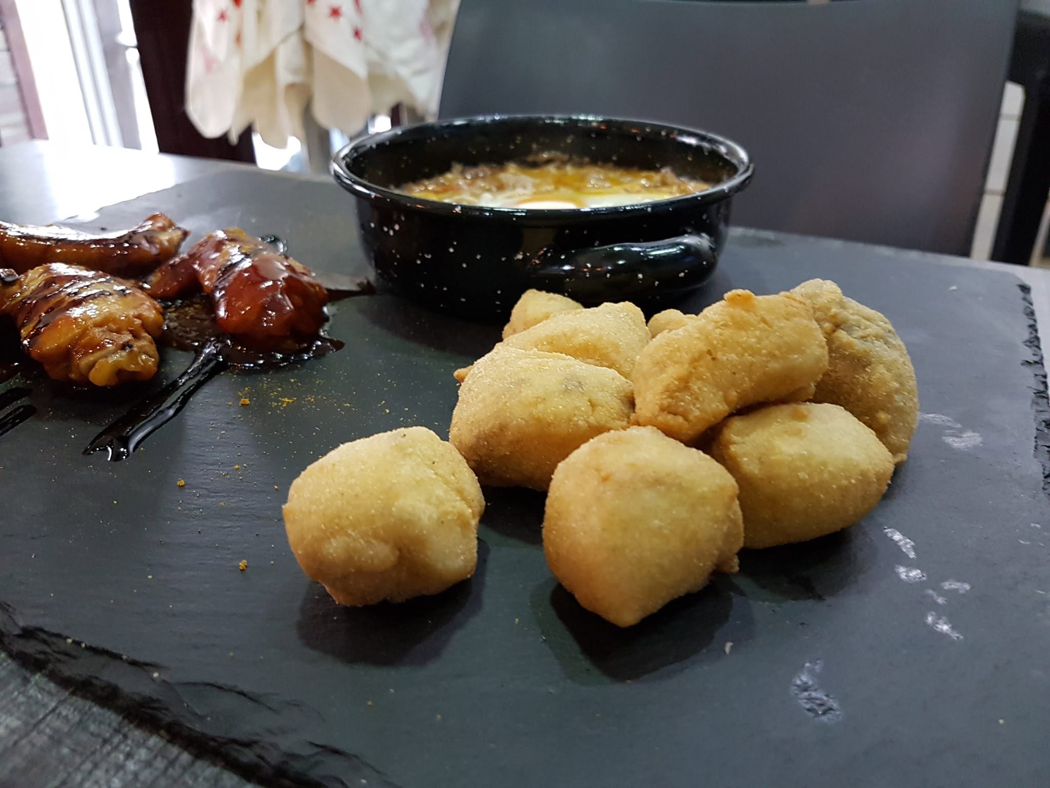 Croquetas caseras, alitas y huevos rotos servidos en pizarra en Cononda